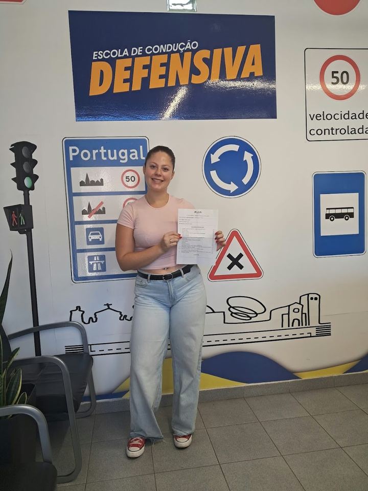 Nova condutora a mostrar o resultado do exame em frente à parede de sinais da escola