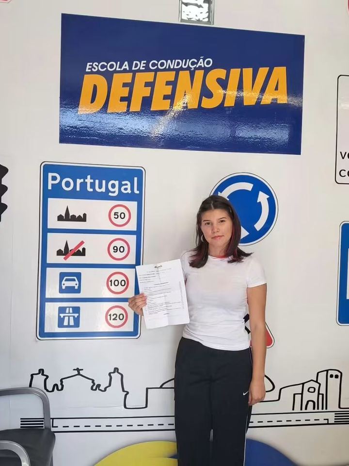 Nova condutora a mostrar o resultado do exame em frente à parede de sinais da escola