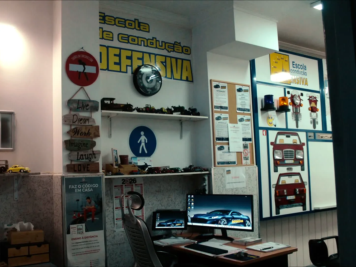Sala de código com o nome da escola na parede, sinais de trânsito e coleção de carros em miniatura